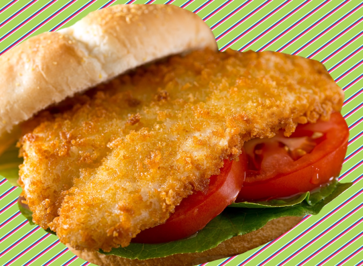 Sanduíche de peixe grelhado em pão integral com alface, tomate e fatias de limão sobre uma mesa de madeira clara