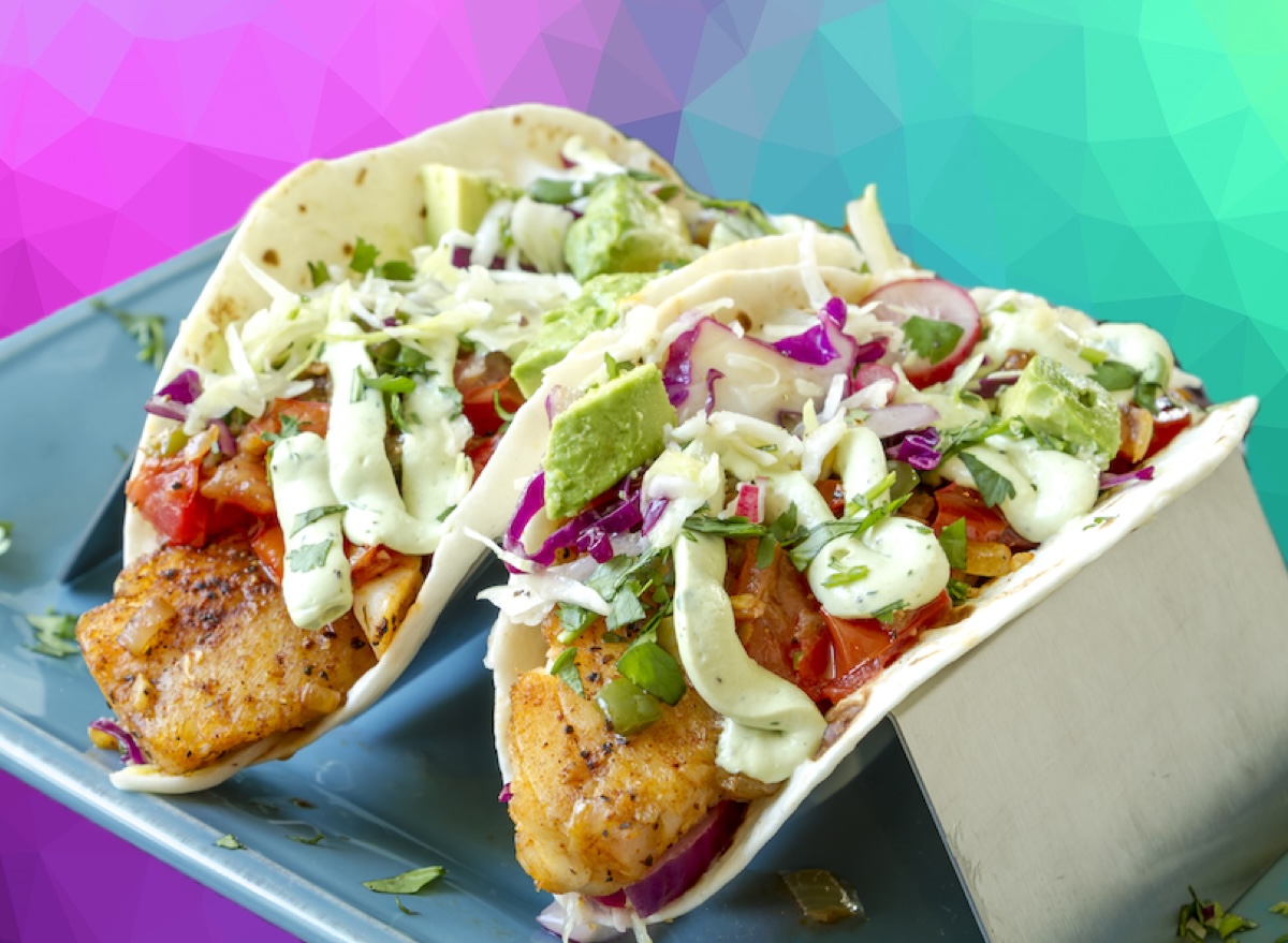 Tacos de peixe fresco com repolho, abacate e limão dispostos sobre uma mesa de madeira em estilo saudável e vibrante