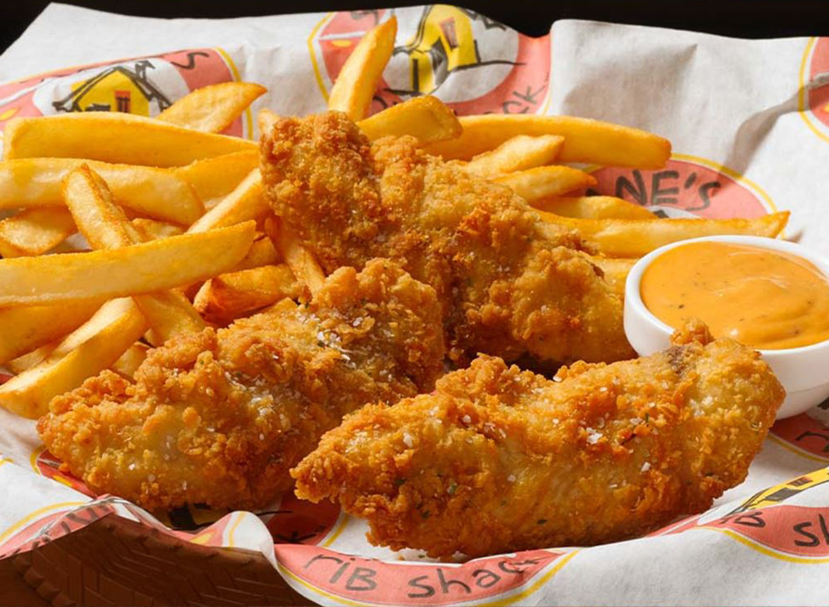 Pedaços de frango frito dourado e crocante dispostos em uma cesta de metal sobre uma mesa de madeira rústica