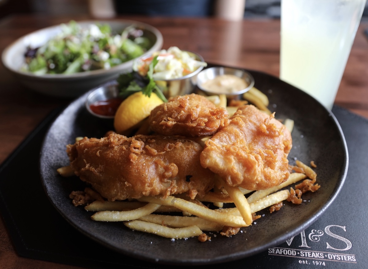Filé de peixe dourado e crocante servido com rodelas de limão e uma salada fresca em um prato de cerâmica