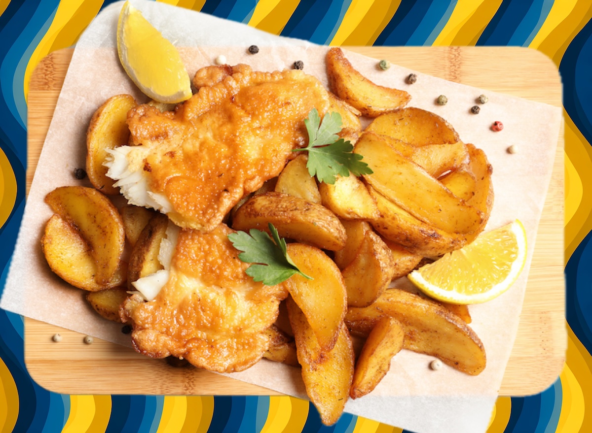 Filé de peixe dourado e crocante sobre uma tábua de madeira, acompanhado de limão fatiado e ervas frescas