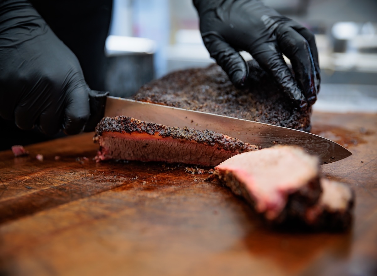 Brisket suculento fatiado em uma tábua de madeira, acompanhado de molho barbecue e salada de repolho ao lado