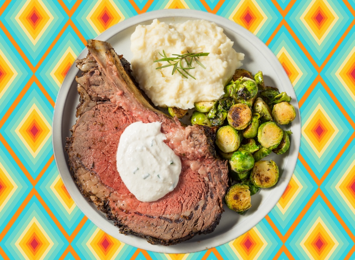 Close em um prime rib cru com marmoreio evidente, sobre uma tábua de madeira ao lado de alecrim e sal grosso
