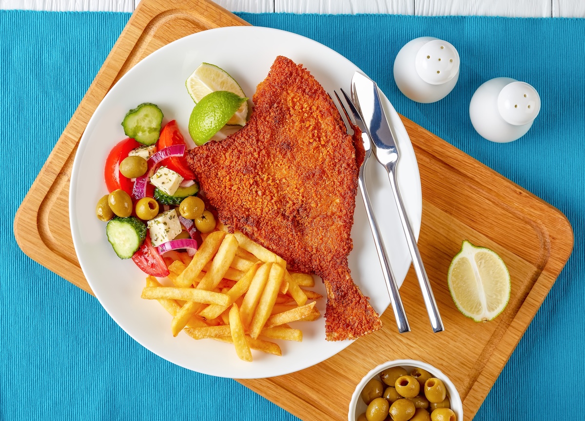 Filé de peixe dourado e crocante servido com rodelas de limão e ervas frescas sobre uma bancada de cozinha rústica