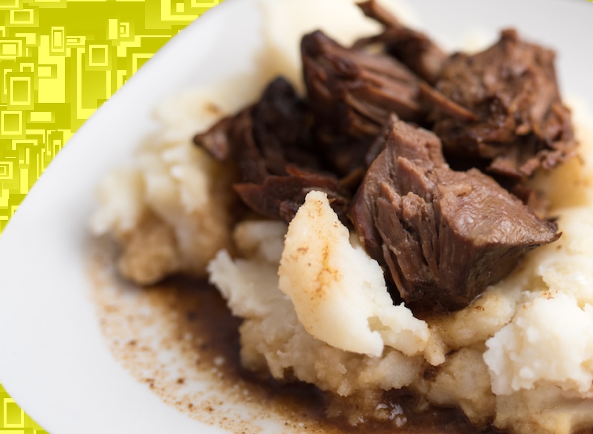 Prato com iscas de carne aceboladas, purê de batatas cremoso e ramos de salsinha fresca sobre uma mesa de madeira