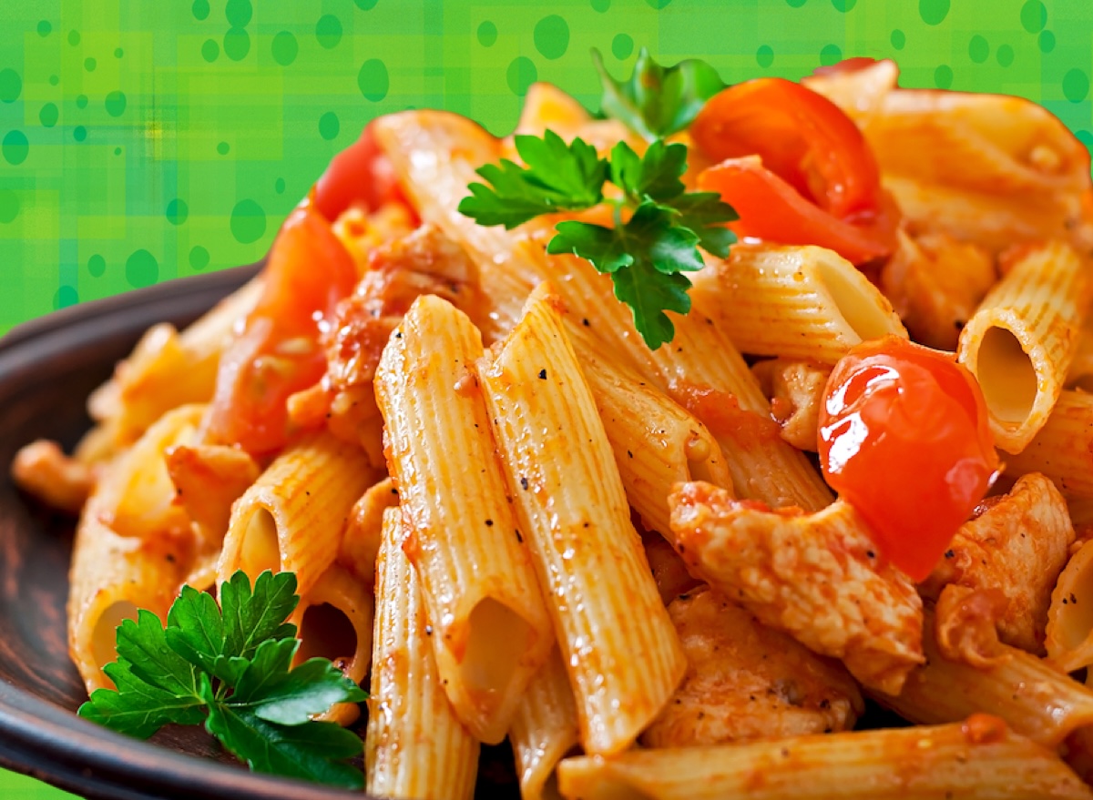Penne al dente em um prato de cerâmica, coberto com molho vermelho, manjericão fresco e um fio de azeite