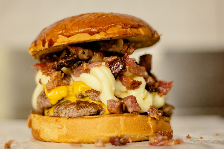 Hambúrguer artesanal com bacon defumado crocante, alface, tomate e queijo, ao lado de uma garrafa de água