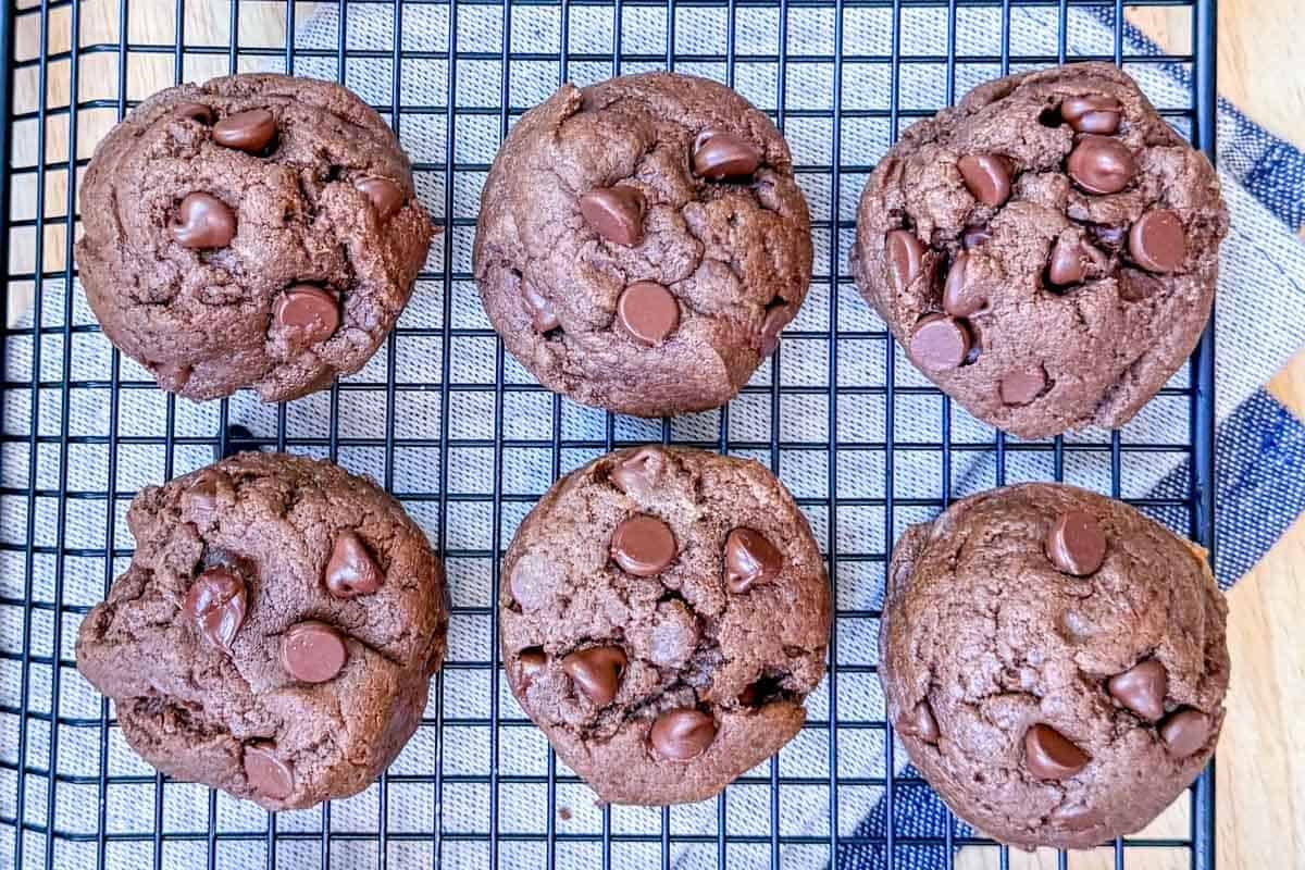 Cookies de proteína com pedaços de chocolate, ao lado de um pote de manteiga de amendoim e um scoop de whey