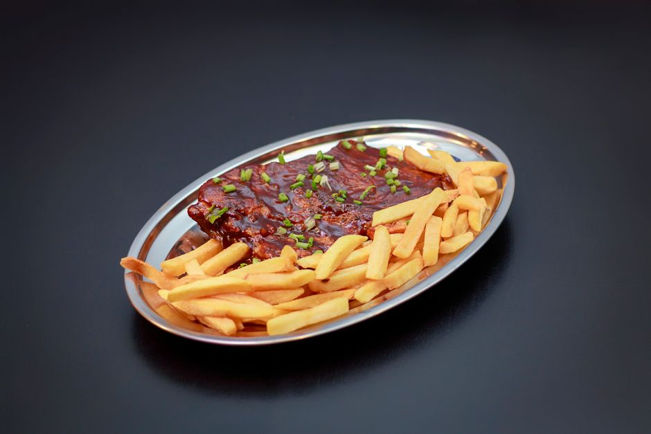 Costela bovina assada lentamente sobre uma grelha, acompanhada de vegetais coloridos e uma tigela de quinoa