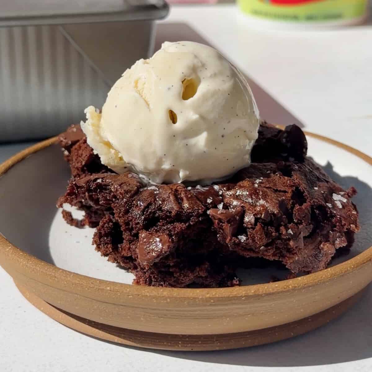 Brownies de chocolate cortados ao meio ao lado de um pote aberto de cottage cheese e uma colher de mel
