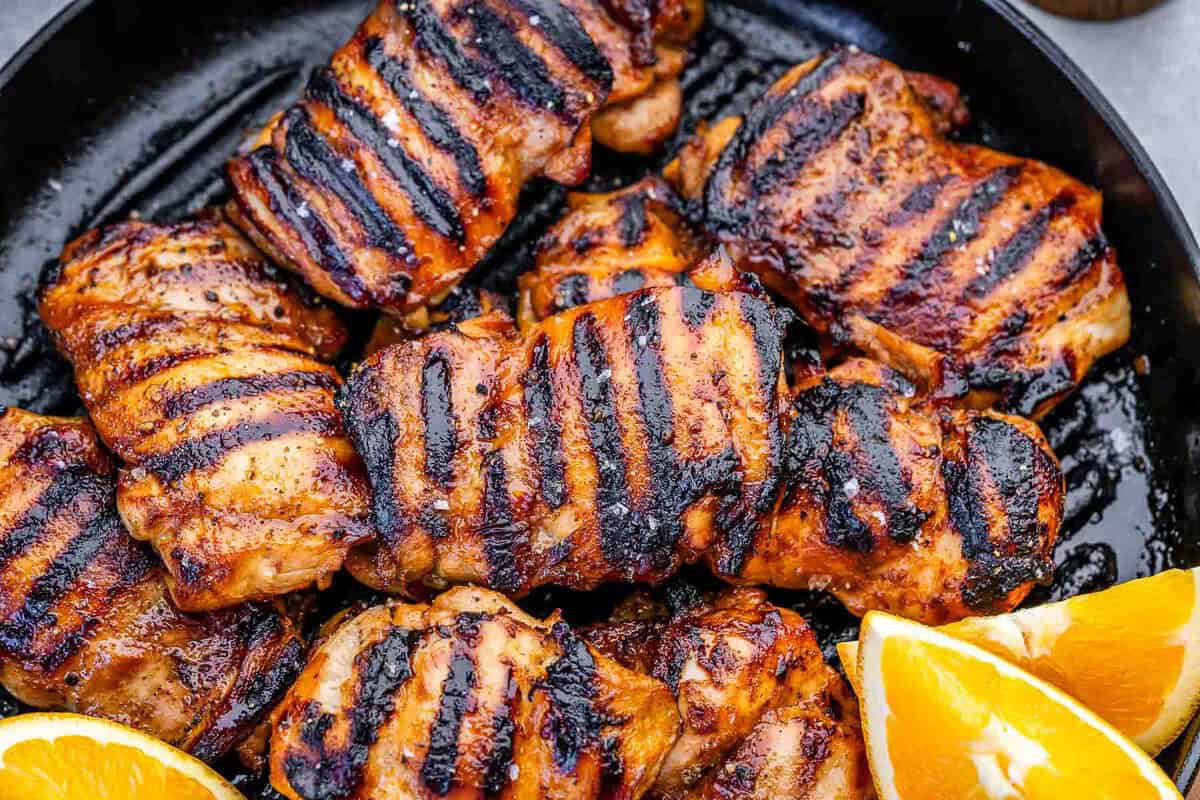 Coxa de frango grelhada com molho cítrico ao lado de limões, brócolis e halteres sobre bancada de madeira
