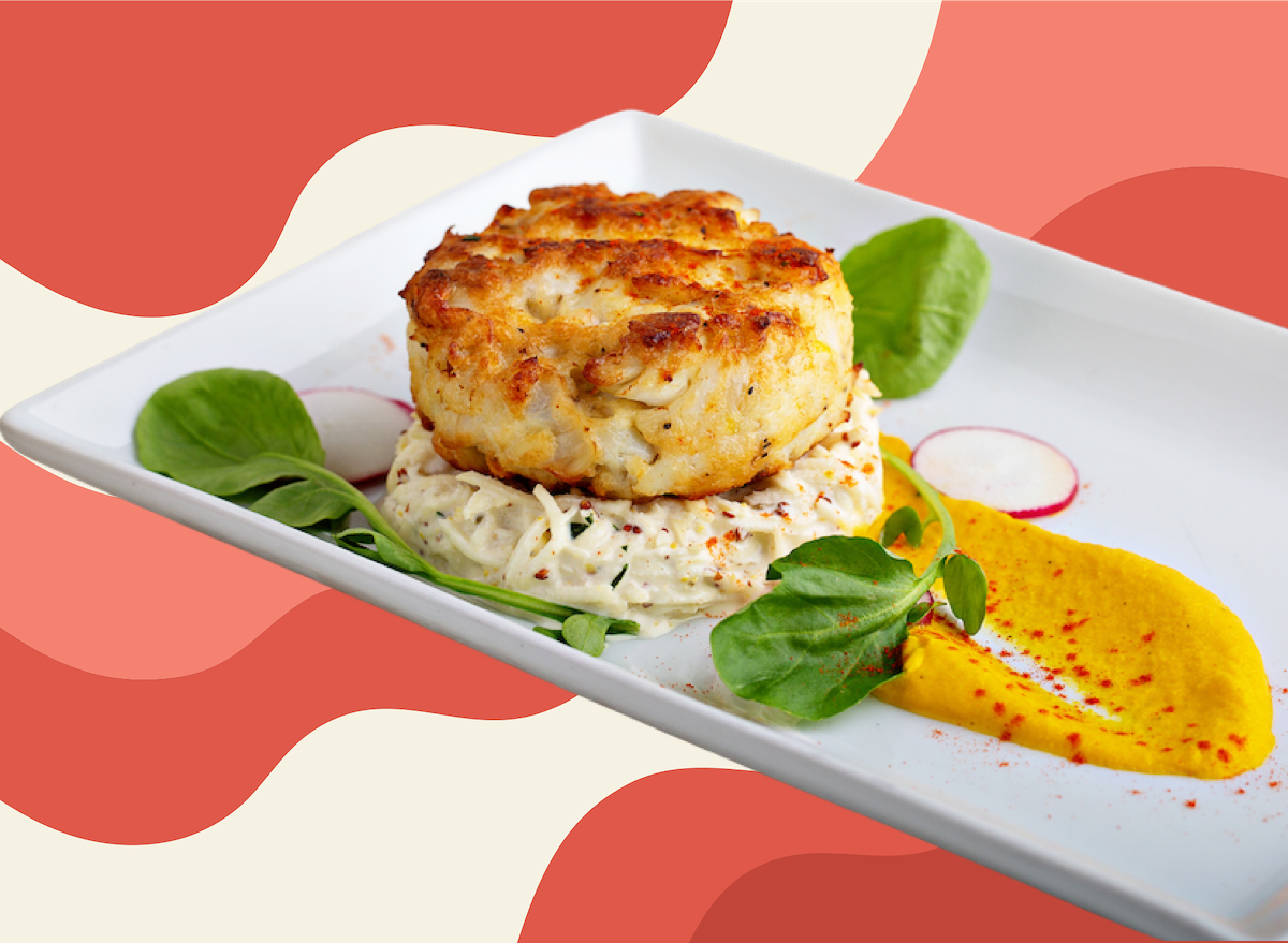 Um prato de crab cake recheado com carne de caranguejo fresca e ervas, ao lado de uma cesta de batatas fritas crocantes