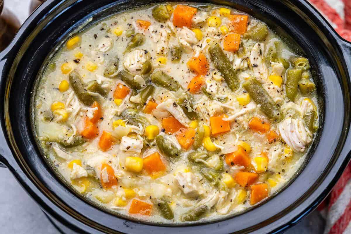 Um crockpot com frango desfiado, legumes e batata cozinhando em um caldo cremoso