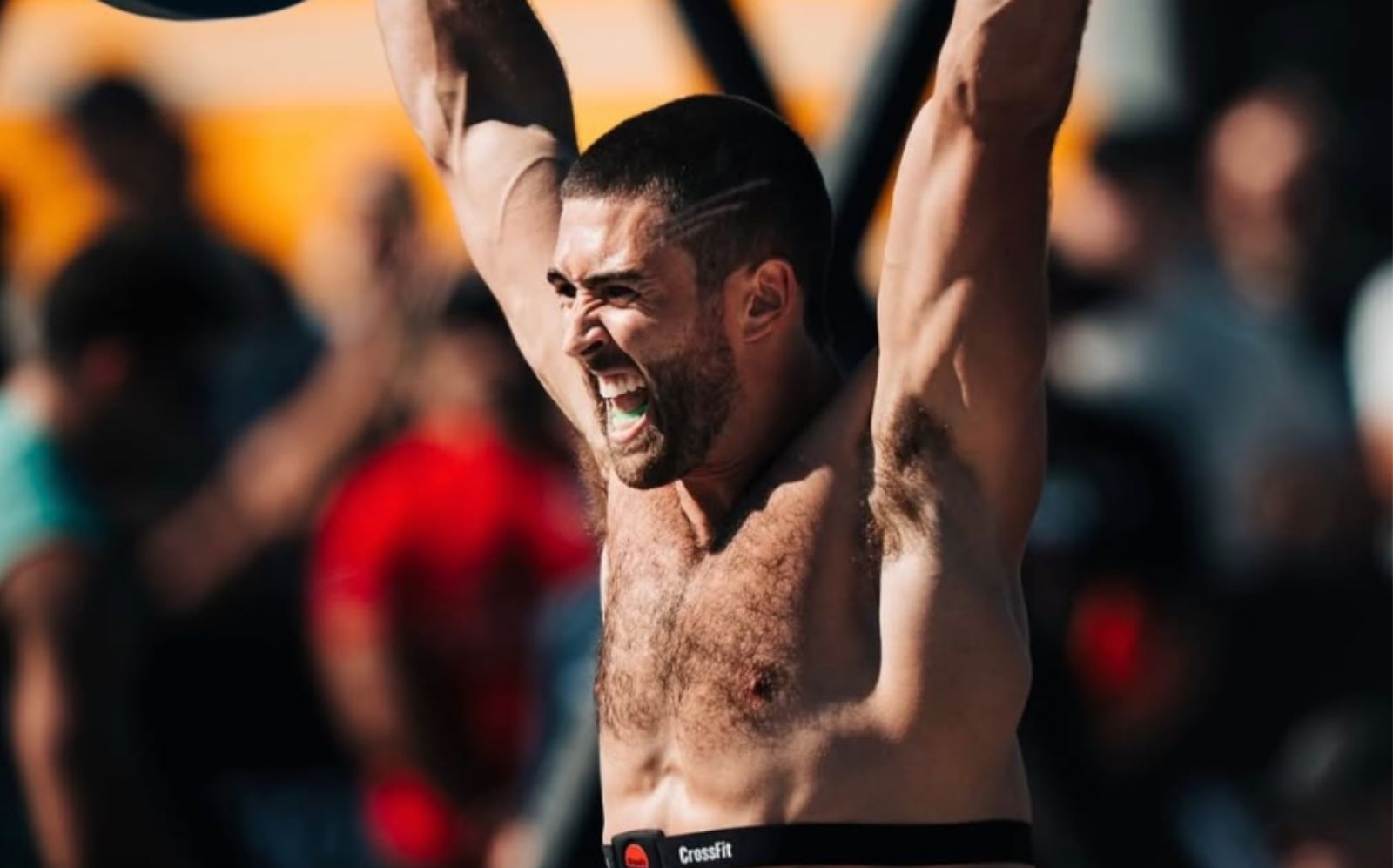 Um atleta masculino em ação, escalando uma parede de corda ao fundo, com um rosto de concentração e um braço esticado para agarrar a corda