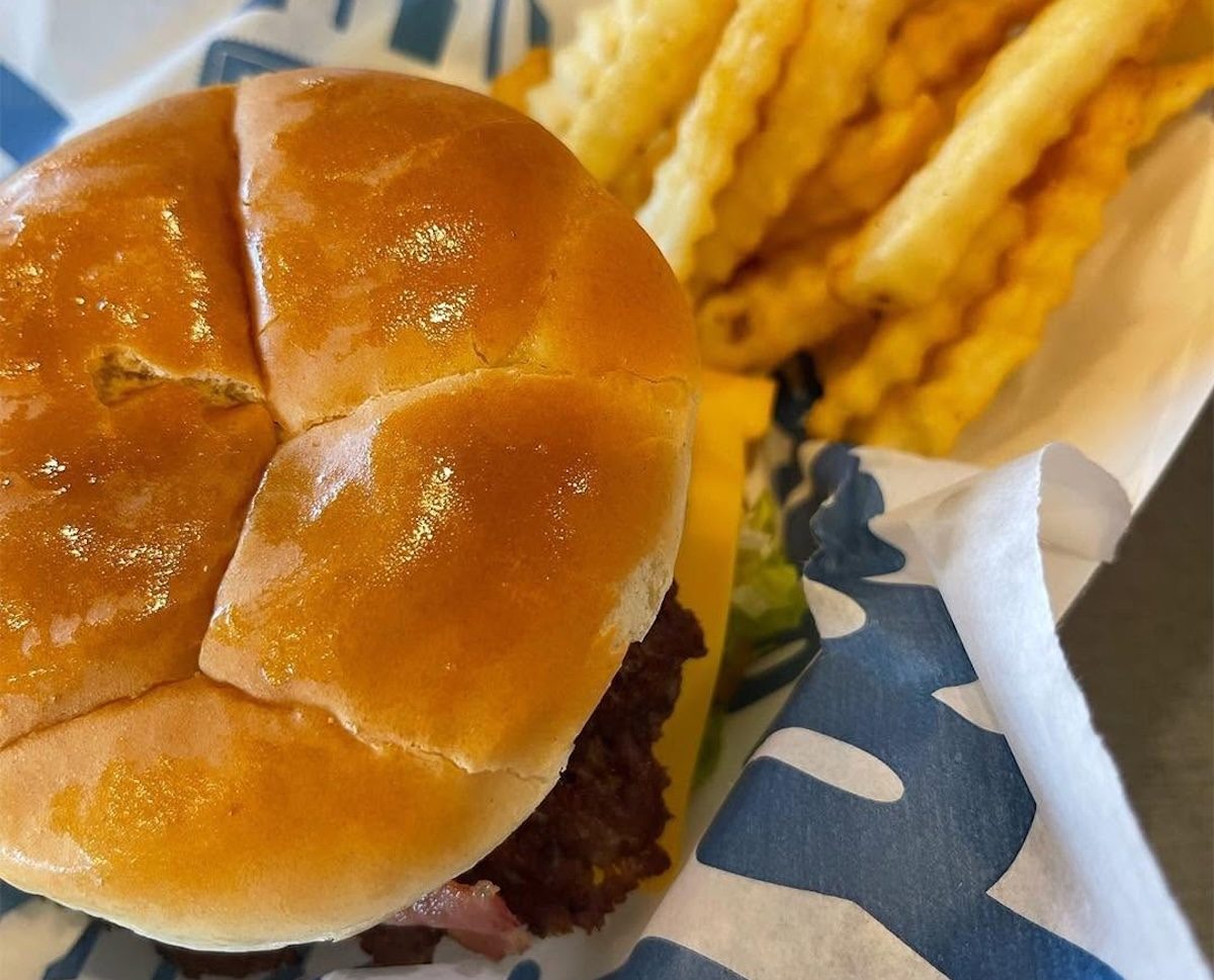 Uma pessoa segurando um sanduíche de frango grelhado e salada em uma embalagem de Culver's, com um copo de água ao lado
