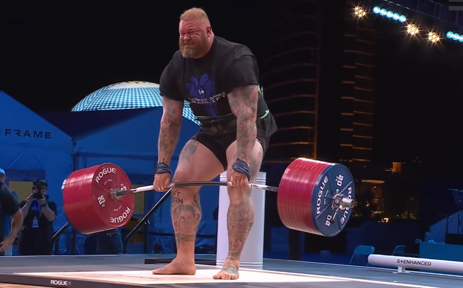 Atleta posicionado para um levantamento terra extremo, segurando uma barra carregada com anilhas em uma academia