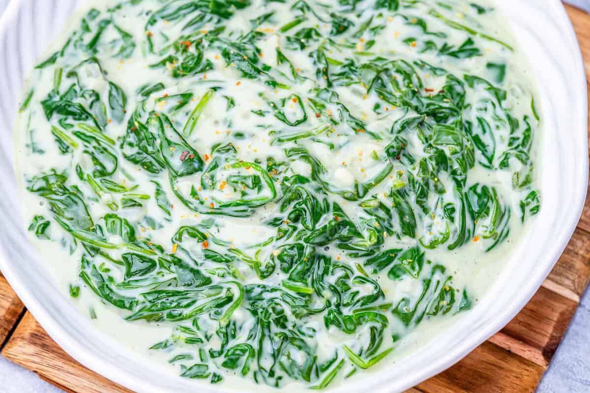 Espinafre verde recém‑cozido em uma frigideira, coberto por molho cremoso branco, com alho picado e pitada de noz‑moscada