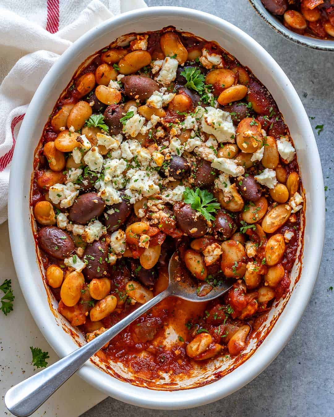 Prato de feijão grego ao forno, com tomate cereja, azeitonas pretas, orégano e fatias de limão ao lado
