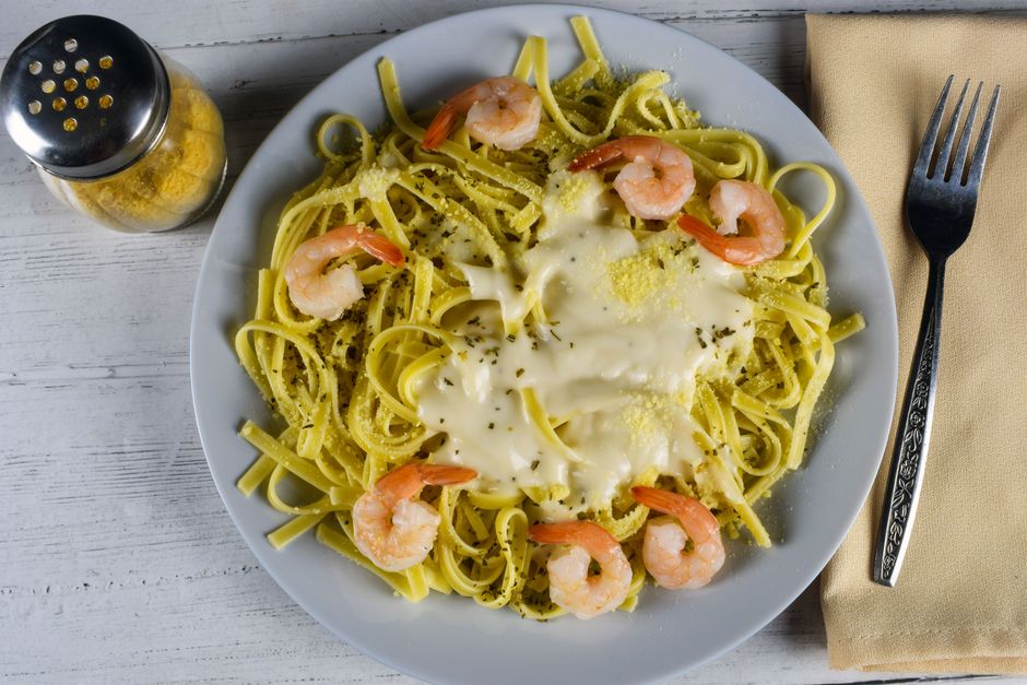 Um prato de fettuccine alfredo caseiro com molho leve, queijo parmesão ralado e vegetais frescos, como cogumelos e espinafre