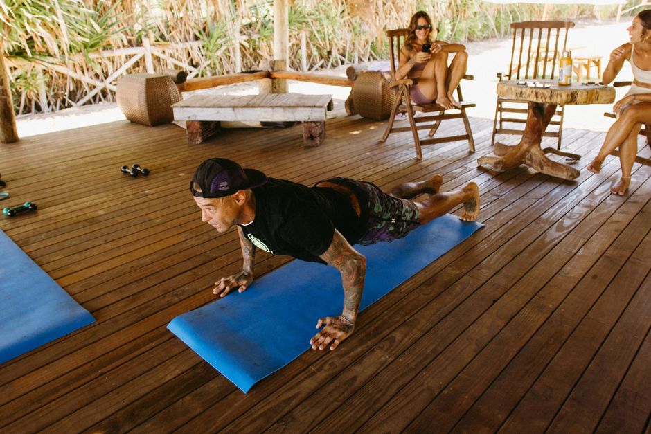 Pessoa de 60+ fazendo flexões no tapete, usando roupa esportiva, com garrafa d'água e relógio fitness ao lado