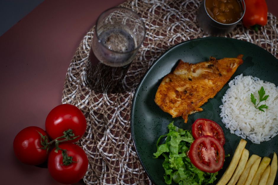 Prato de frango à milanesa dourado, empanado crocante, ao lado de salada verde e limão, sobre tábua de madeira