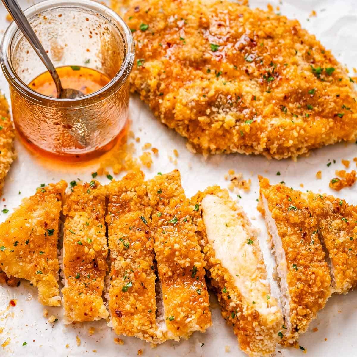 Pedaços de frango dourados com crosta de panko dispostos em uma travessa ao lado de um pote de mel e azeite