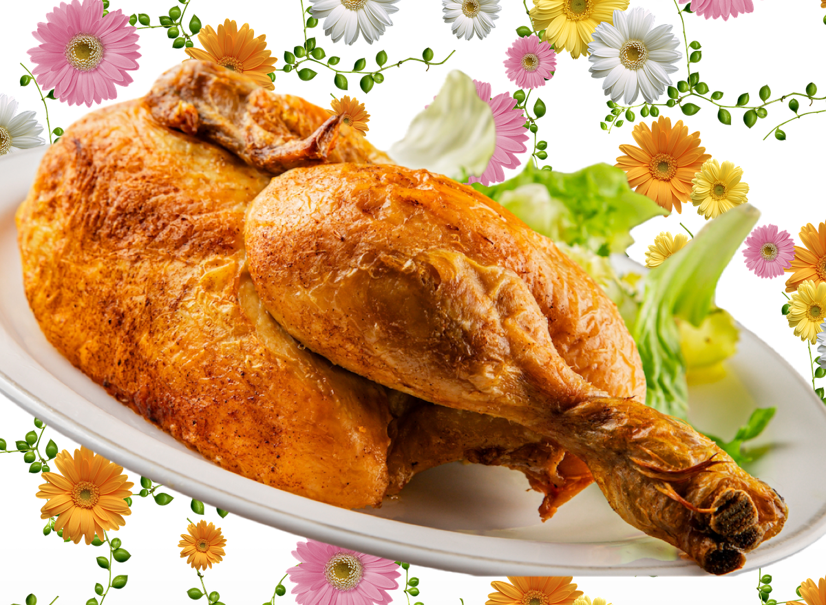 Prato de frango assado dourado ao lado de legumes coloridos e um garfo sobre tábua de madeira