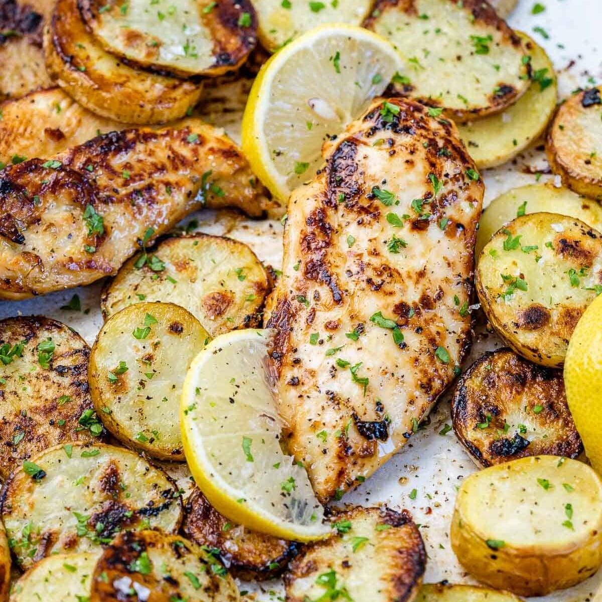 Frango grelhado com batatas assadas, rodelas de limão e ervas frescas dispostos em uma assadeira rústica