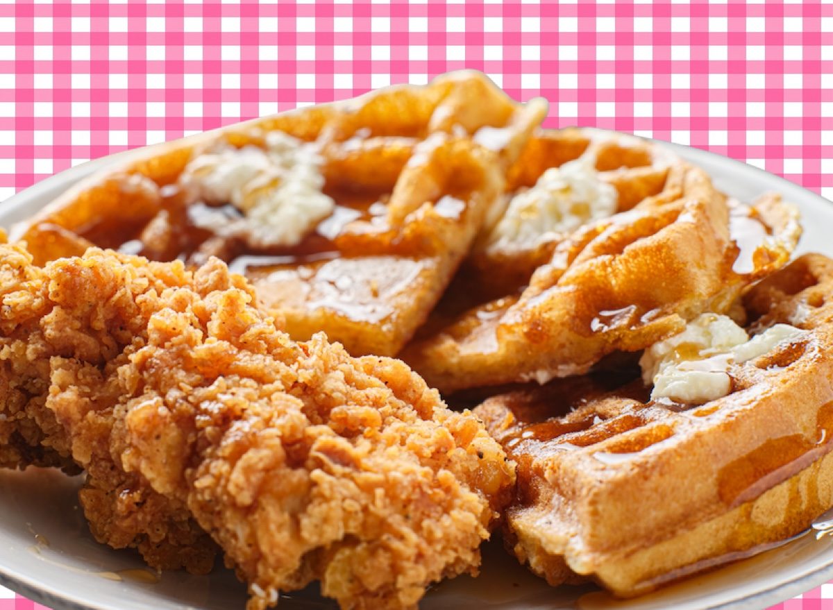 Um prato de frango empanado crocante ao lado de waffles macios e um copo de suco de frutas frescas