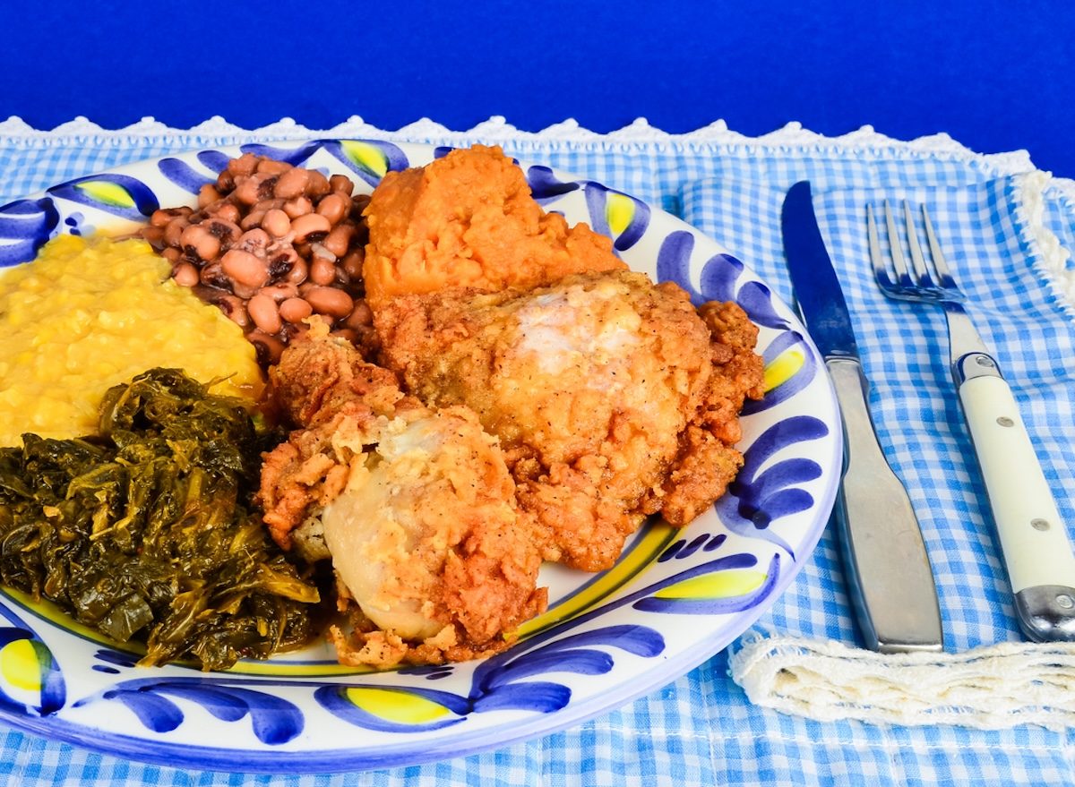 Frango frito dourado ao lado de feijão-fradinho cozido, salada verde e garrafa de água sobre mesa rústica