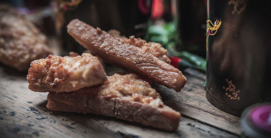 Frango frito dourado ao lado de torradas de alho crocantes, com alecrim, limão e um copo de água gelada sobre a mesa