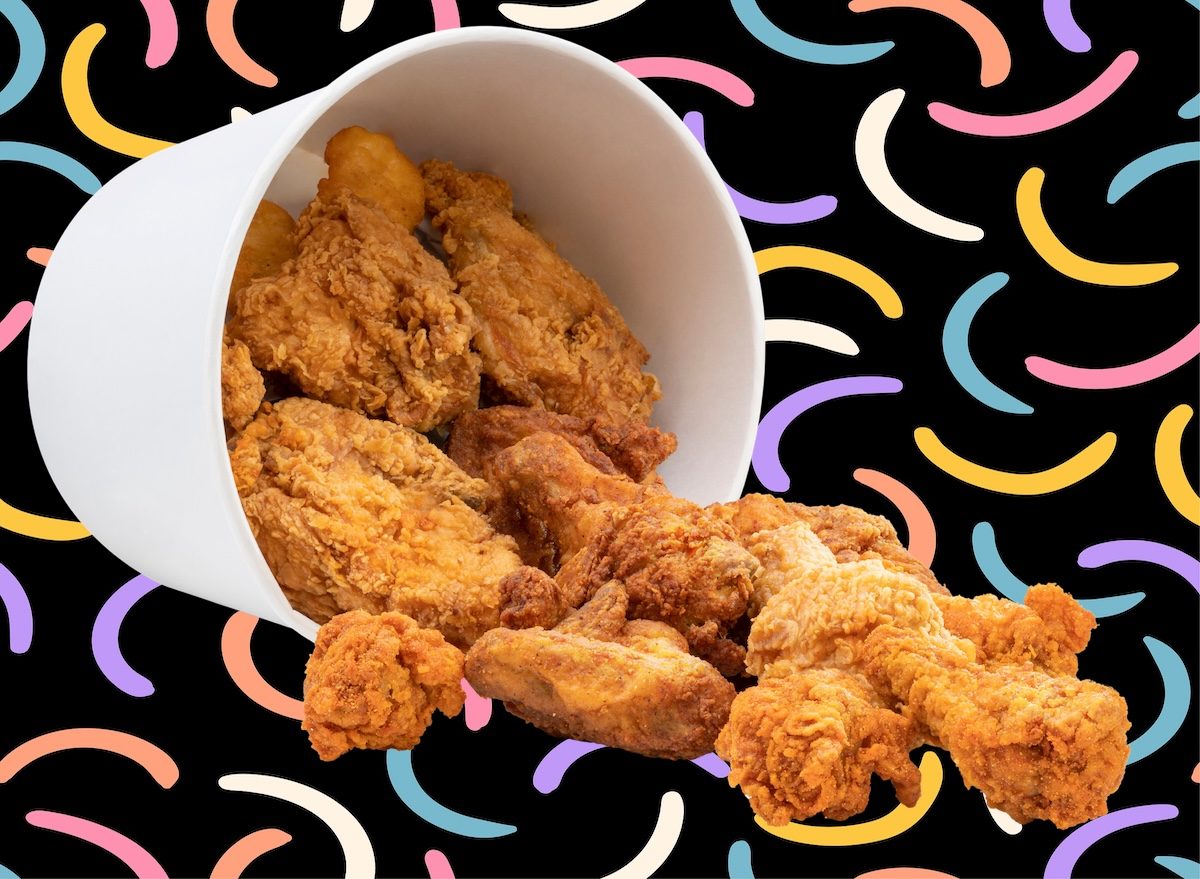 Um frango frito crocante com pele dourada e uniforme, servido em uma bandeja de madeira com folhas de alface fresca