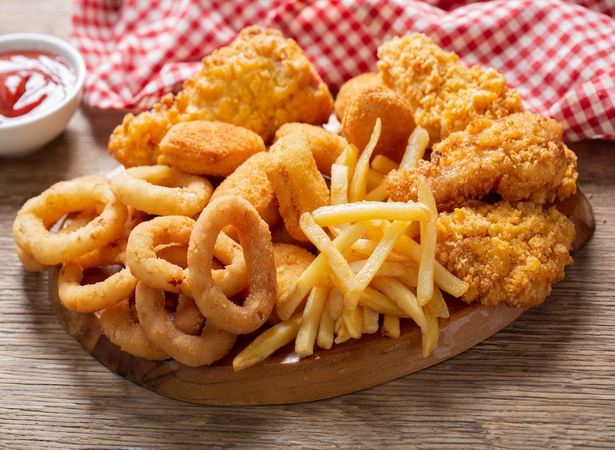 Prato com pedaços de frango frito dourado ao lado de onion rings crocantes, acompanhados de limão e molho