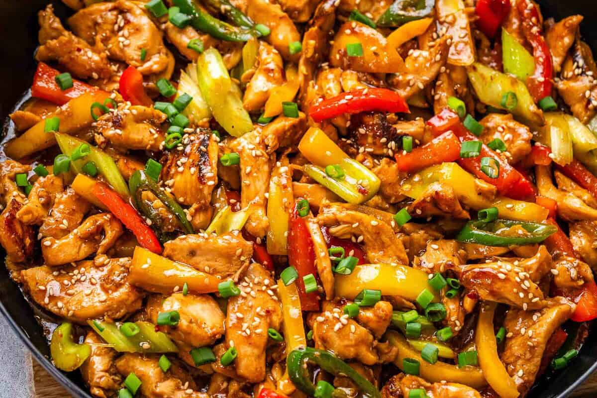 Tigela de frango salteado com brócolis e pimentões coloridos sobre uma mesa de madeira com hashis ao lado