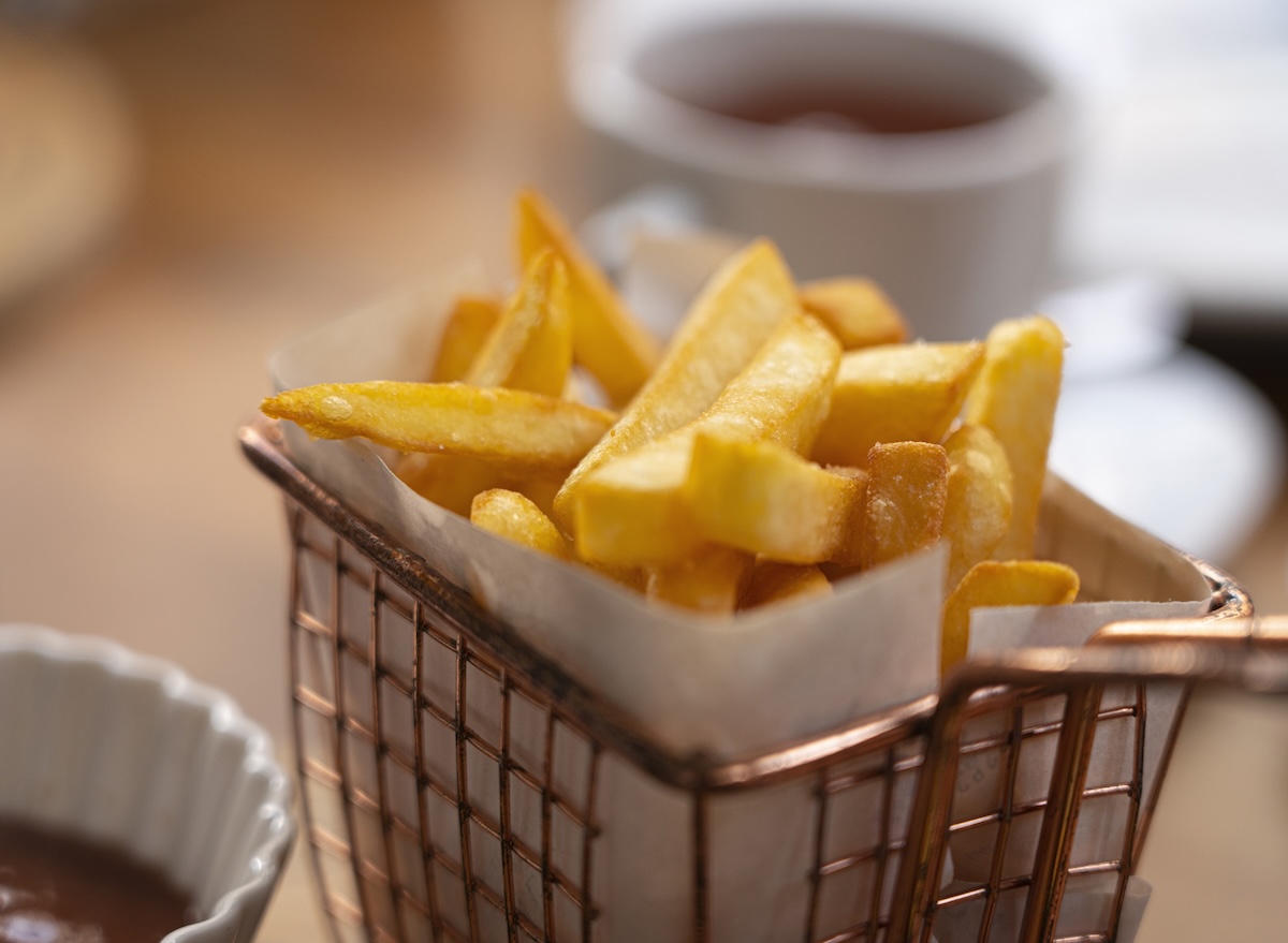 Uma batata frita crocante, com textura crocante na superfície e maciez interior, é ilustrada ao lado de um prato de salada verde