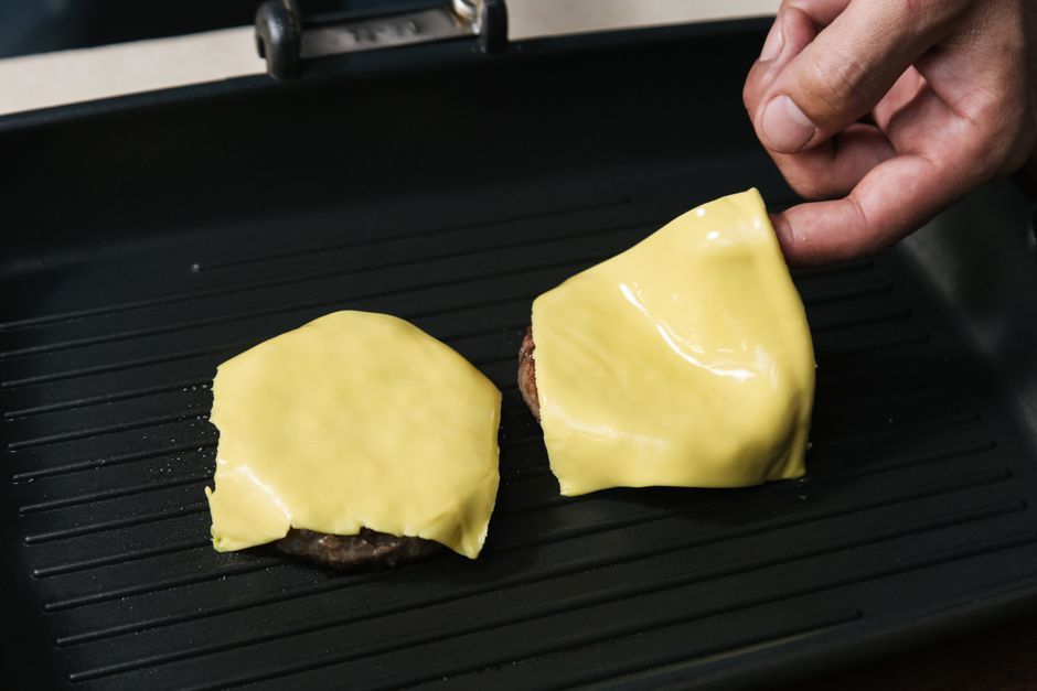 Um cheeseburger congelado em uma grelha de cozinha, com aditivos e gordura trans destacados em uma legenda