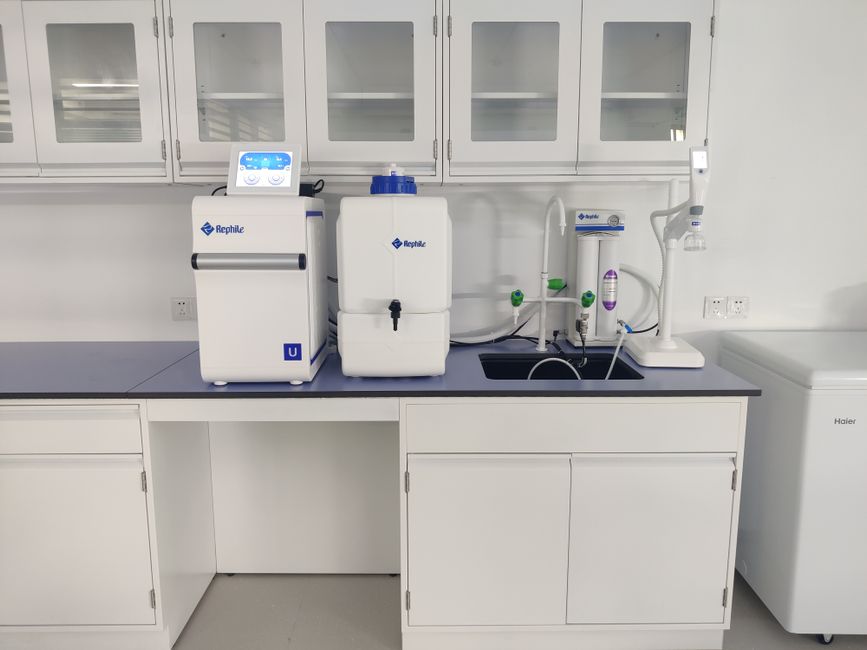 Mão segurando colher de aço inox sobre pó multivitamínico colorido ao lado de um frasco de premix