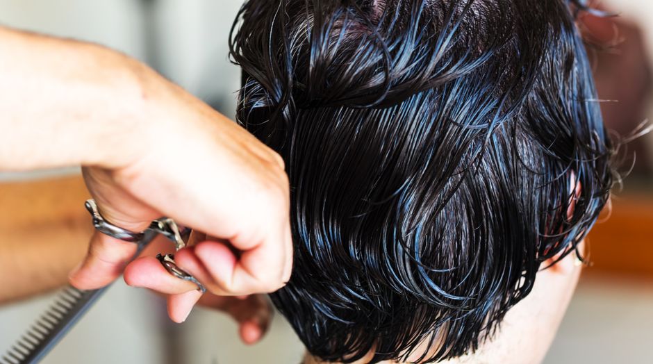 Uma mulher com cabelo fino e descolorido, segurando um copo de suco de vegetais, ao lado de um frasco de suplemento com o rótulo AnaGain
