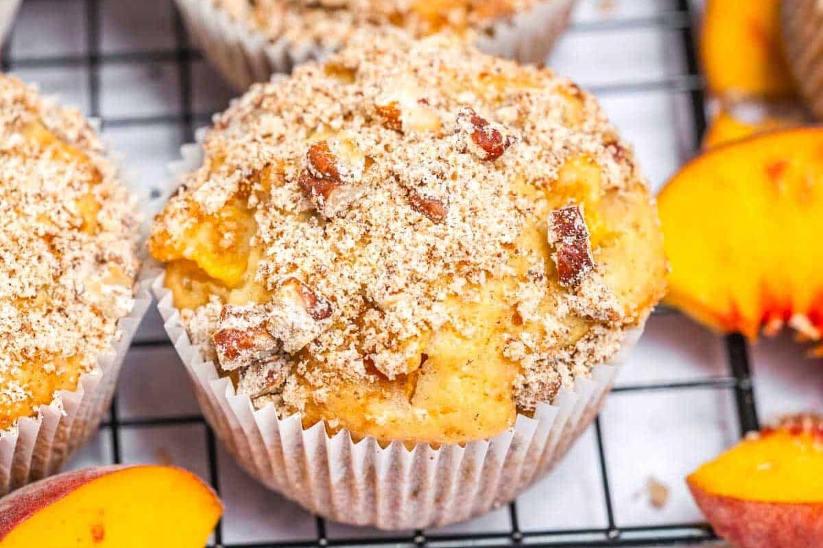 Muffins dourados de iogurte grego com pedaços de pêssego ao lado de uma tigela de iogurte e frutas frescas