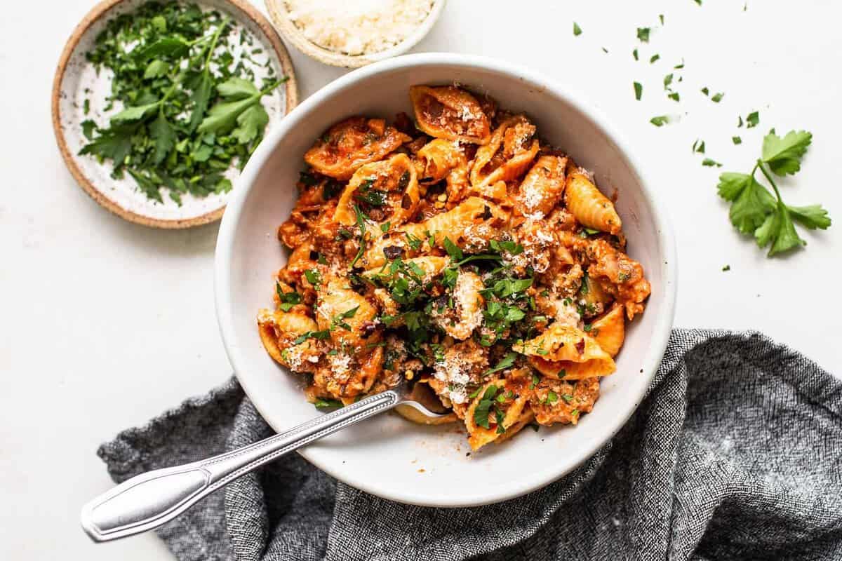 Prato de macarrão integral com carne de peru moída, tomate cereja e espinafre ao lado de uma colher medindo proteína