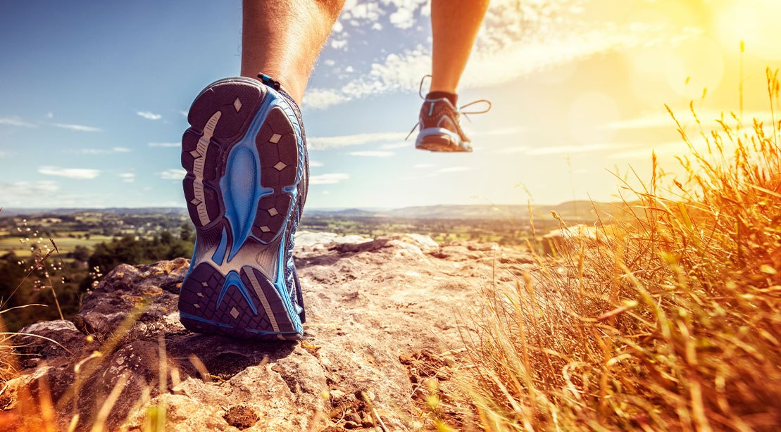 Uma pessoa correndo em trilha, com o Hoka Speedgoat 7 no pé, sob o sol de um dia de verão