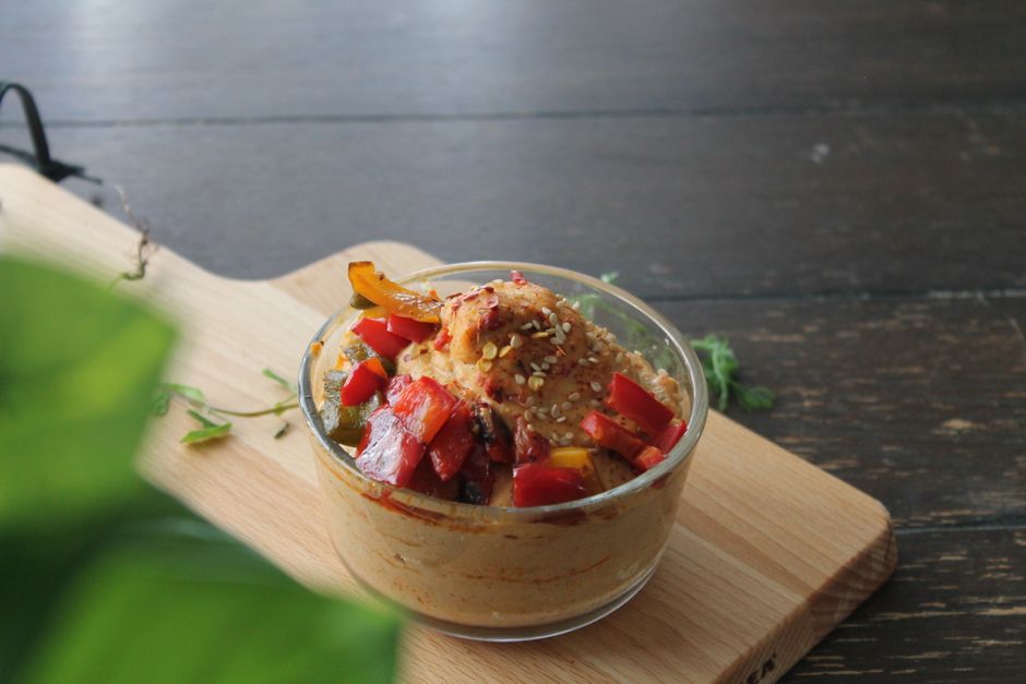 Uma pessoa segurando uma colher de sopa de hummus orgânico, ao lado de frutas e vegetais frescos