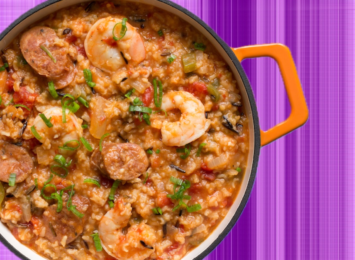 Panela de ferro com jambalaya colorido, contendo camarões, linguiça e vegetais frescos sobre uma mesa de madeira