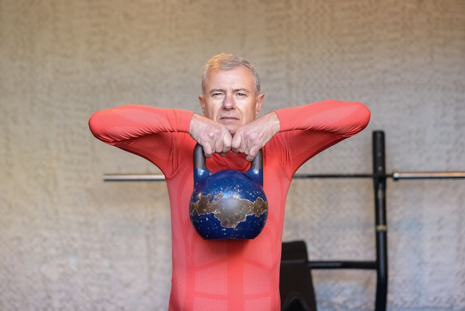 Uma pessoa segurando uma kettlebell, com uma expressão de esforço, realizando um deadlift