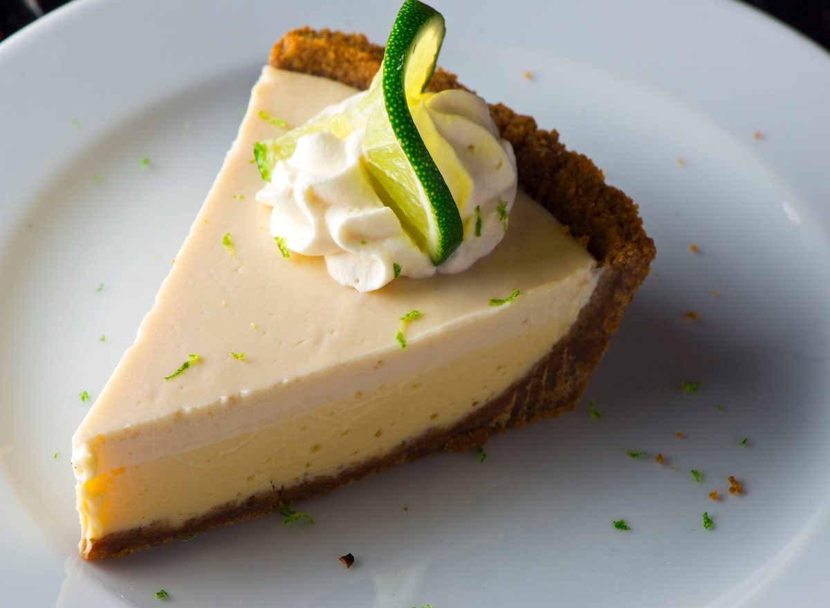 Pessoa sorridente segurando uma torta de key lime e uma folha de limão-cravo