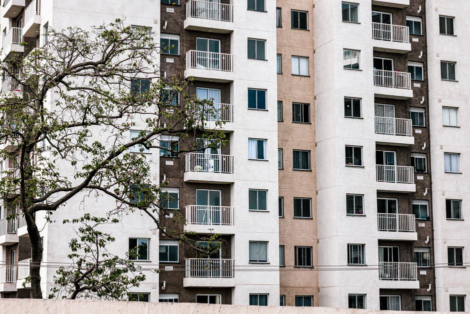 Idosa usando apoio no balcão enquanto faz elevação de perna com faixa elástica e garrafa de água ao lado