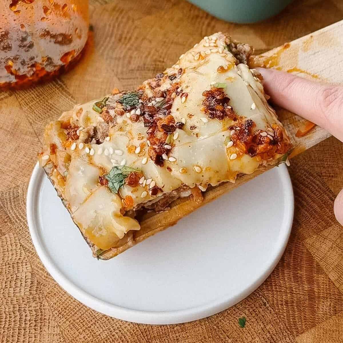 Camadas de lasanha com folhas de wonton, carne moída, cenoura em tiras e cebola verde sobre prato branco