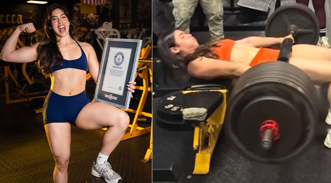 Lilian Zamora segurando uma barra carregada com discos pesados enquanto realiza hip thrust em academia iluminada