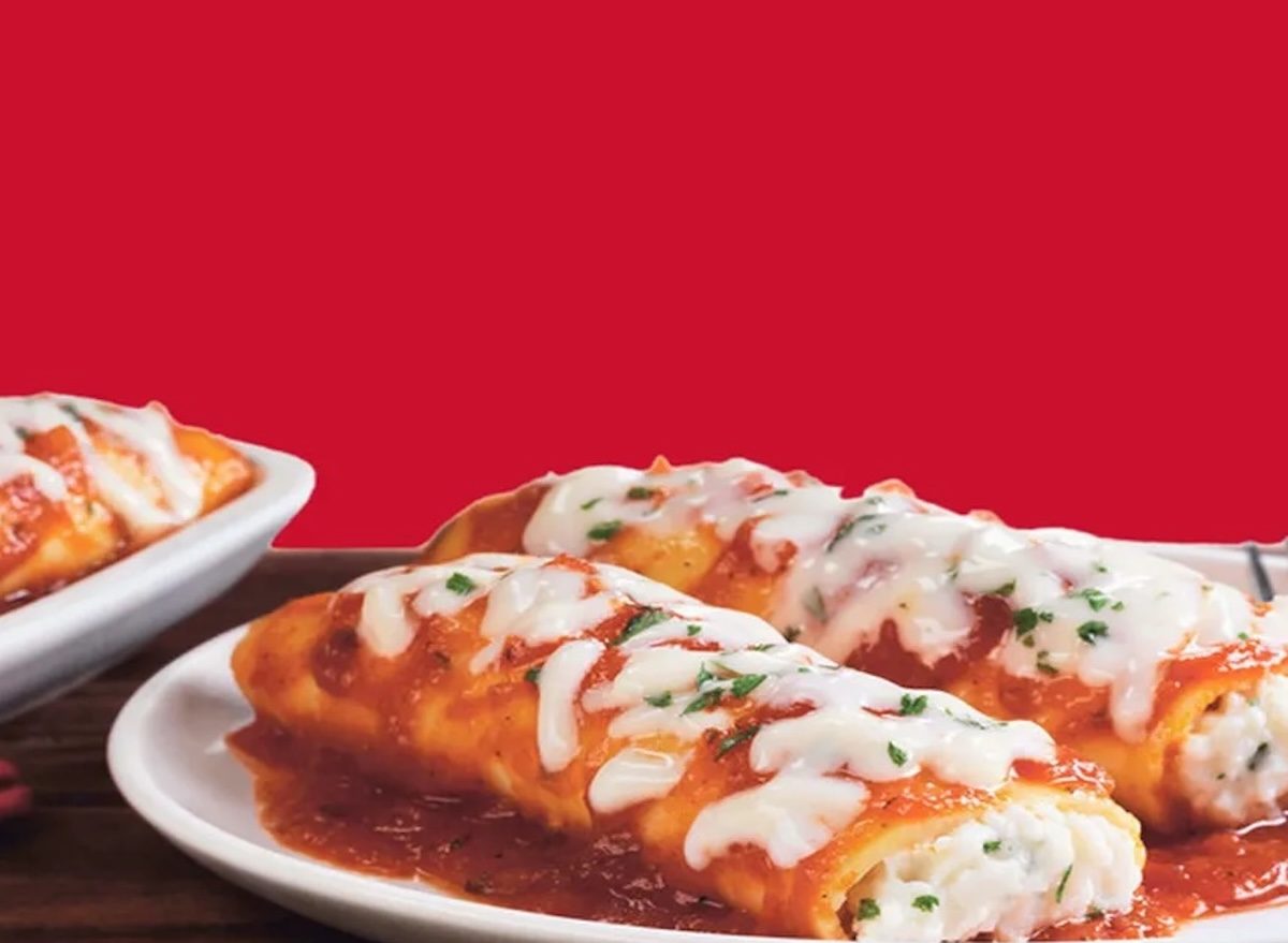Uma mulher prepara um prato de manicotti congelado reaquecido com vegetais frescos e um copo de água
