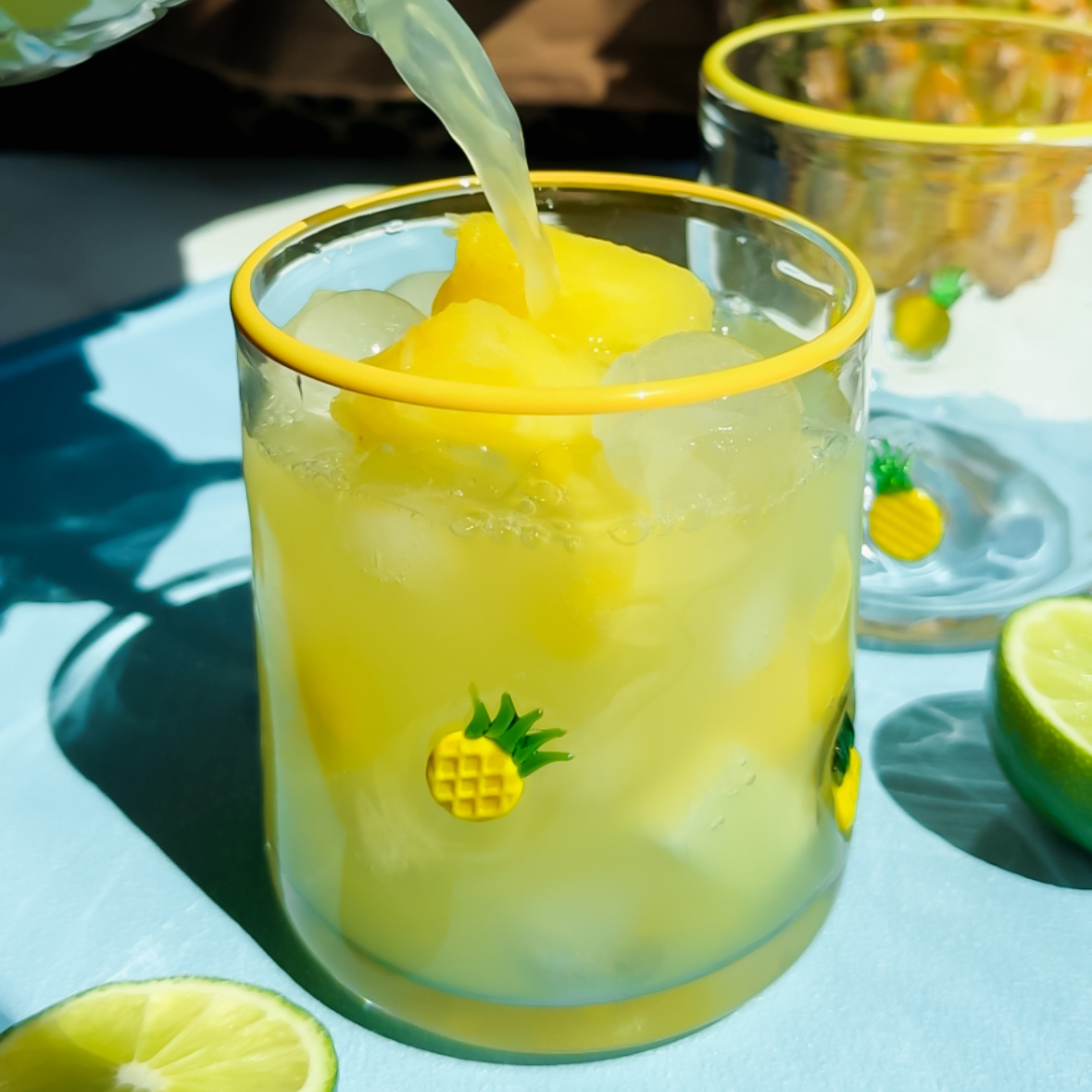 Taça de margarita com abacaxi fresco, gelo e uma rodela da fruta na borda, sobre uma mesa em ambiente ensolarado